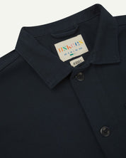 Close-up top-half view of #3001, dark blue (blueberry) organic cotton drill overshirt. With focus on collar, Uskees brand label and corozo buttons.