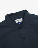 Close-up view of 3001 blueberry, buttoned ripstop overshirt from Uskees showing corozo buttons, brand label, collar and hanging hoop.