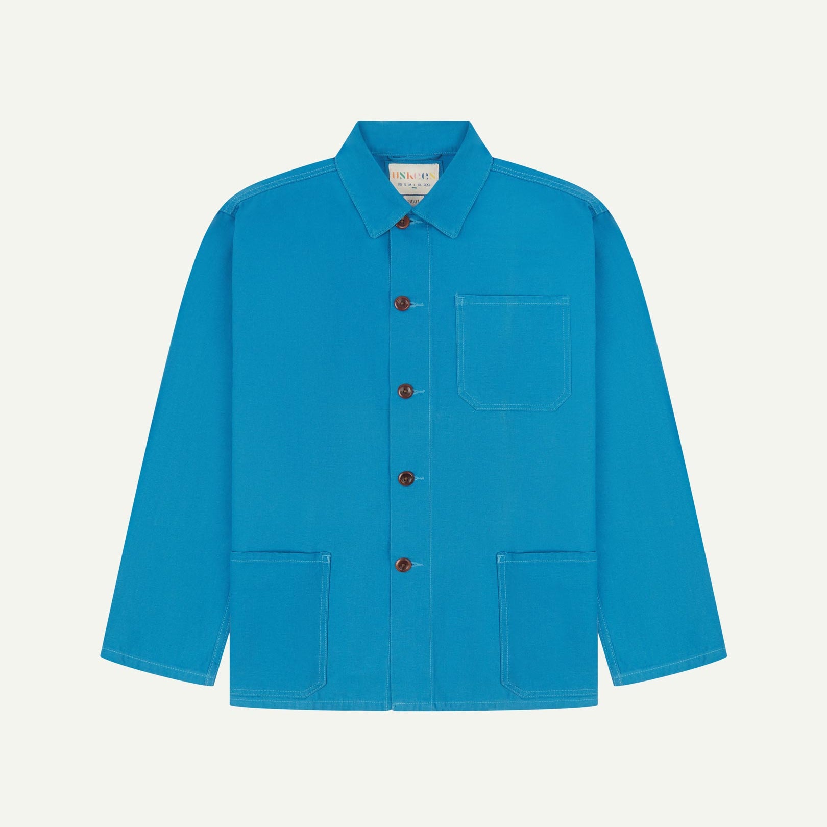 Front flat shot of bright blue, buttoned organic cotton overshirt. Clear view of chest and hip pockets, corozo buttons and Uskees branding label.