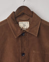 Close-up, top-half front view of brown-coloured corduroy overshirt on hanger showing collar with top button fastened and Uskees label.
