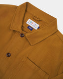 Close-up top-half view of #3001 buckthorn (mustard yellow) organic cotton drill overshirt. With focus on collar, Uskees brand label and corozo buttons.
