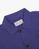 Close-up view of 3001 purple, buttoned organic cotton overshirt from Uskees showing corozo buttons, branding label, collar and hanging loop.