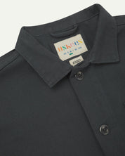 Close-up top-half view of #3001, charcoal-grey organic cotton drill overshirt. With focus on collar, Uskees brand label and corozo buttons.