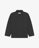 Front flat shot of charcoal-grey, buttoned organic cotton overshirt. Clear view of chest and hip pockets, corozo buttons and Uskees branding label.