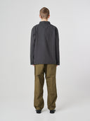 Full-length back view of man wearing an Uskees charcoal-grey cotton overshirt paired with khaki-green pants, showing reinforced elbows.