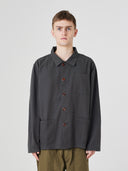 Top-half view of man wearing an Uskees charcoal-grey cotton overshirt indicating roomy, boxy fit with clear view of deep pockets on the chest and front.