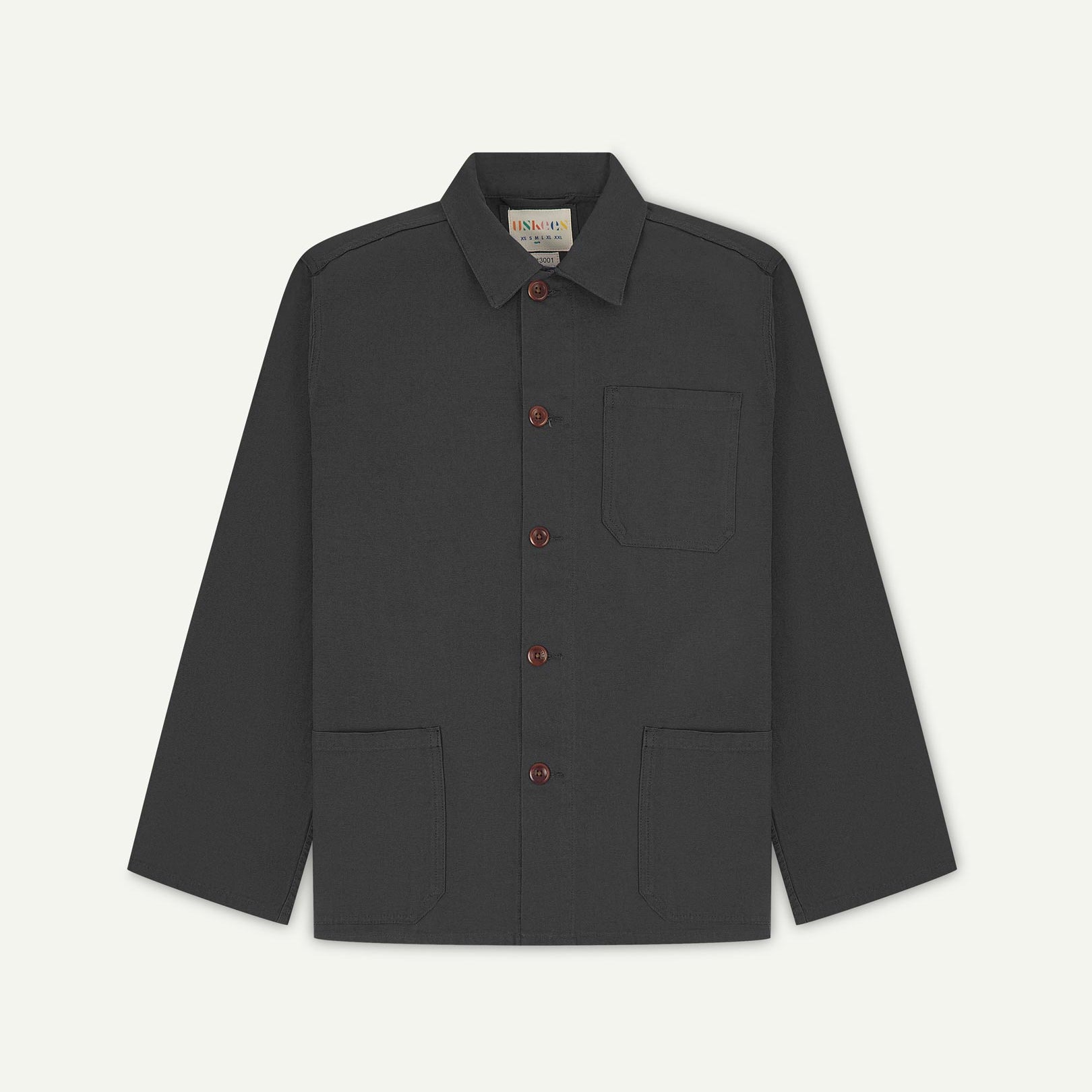 Front flat shot of charcoal-grey, buttoned organic cotton overshirt. Clear view of chest and hip pockets, corozo buttons and Uskees branding label.
