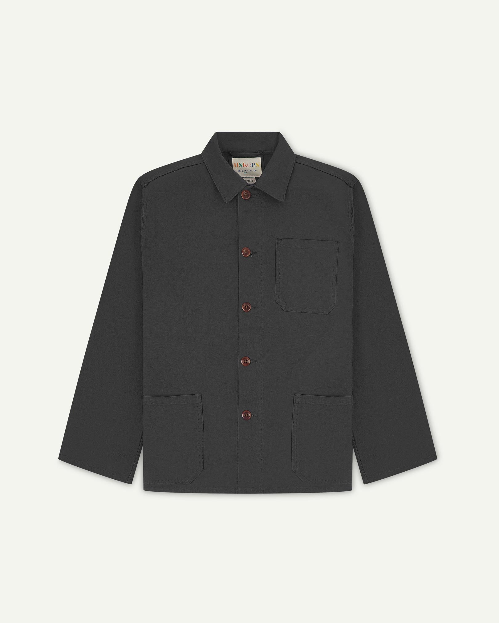 Front flat shot of charcoal-grey, buttoned organic cotton overshirt. Clear view of chest and hip pockets, corozo buttons and Uskees branding label.