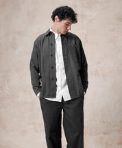 Model wearing Uskees men's shirt jacket, illustratiing the boxy design and paired with white shirt and dark pants.