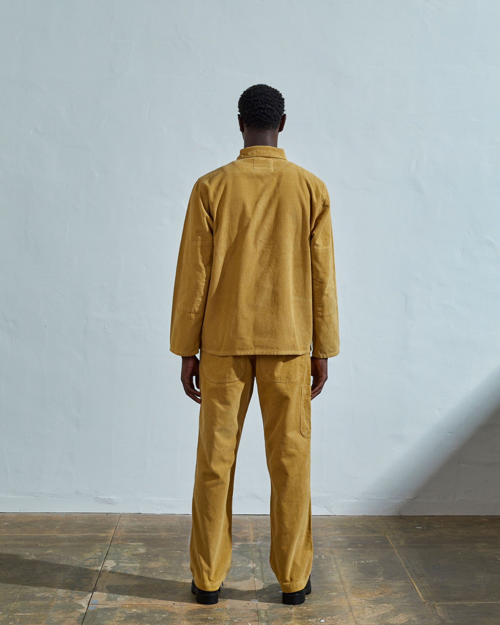 Full-length reverse view of model wearing #3001, citronella-yellow corduroy overshirt with view of reinforced elbow area and demonstrating boxy silhouette.