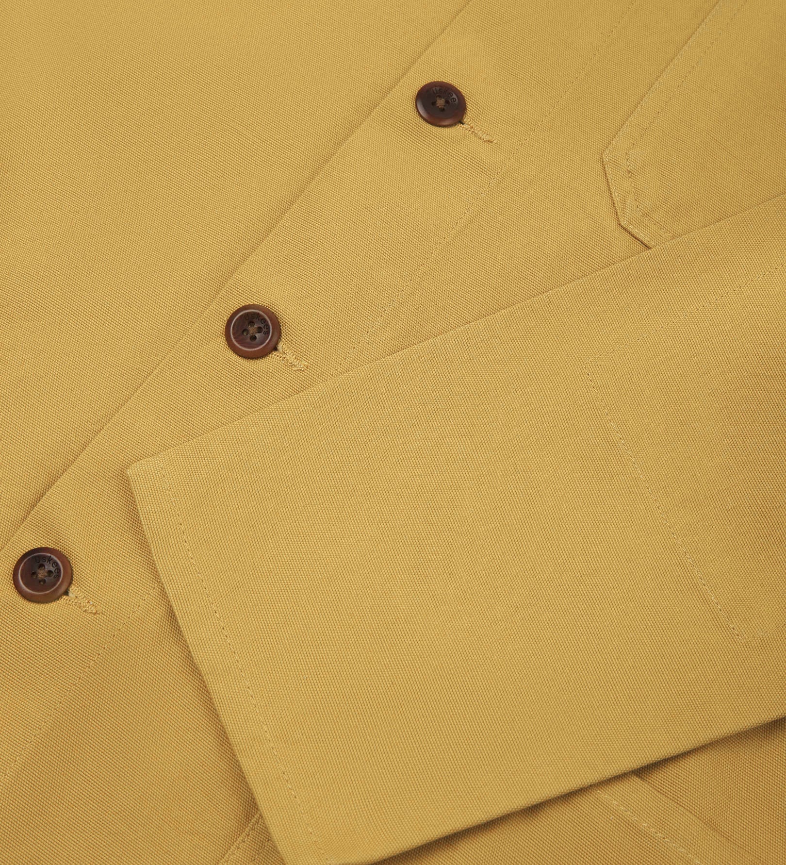 Closer view of mid section of yellow (citronella), buttoned organic cotton overshirt from Uskees. Focus on cuff, pockets and corozo buttons.