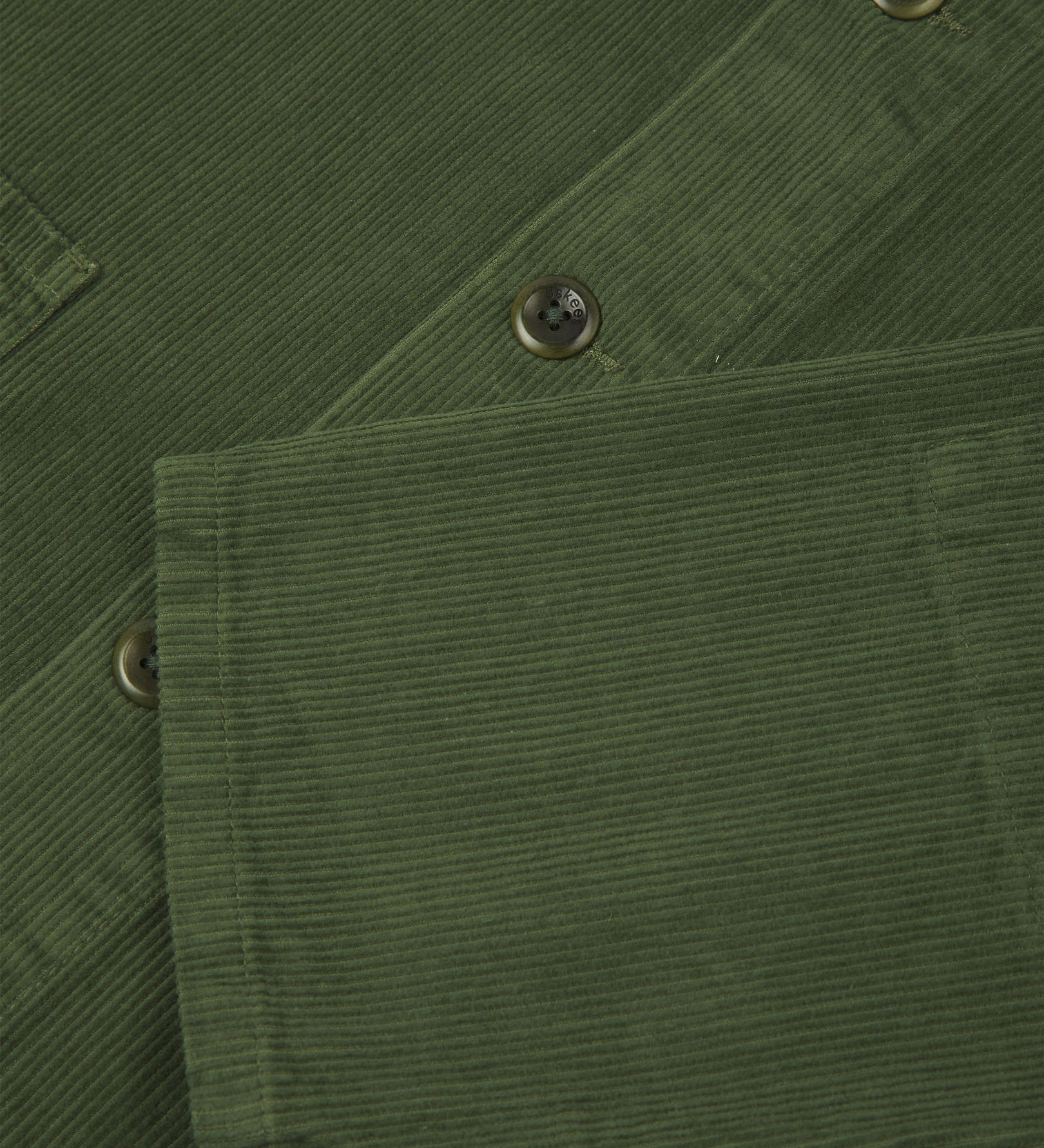 Closer view of mid section of coriander-green, buttoned corduroy overshirt from Uskees. Focus on cuff, pockets, corozo buttons and corduroy texture.
