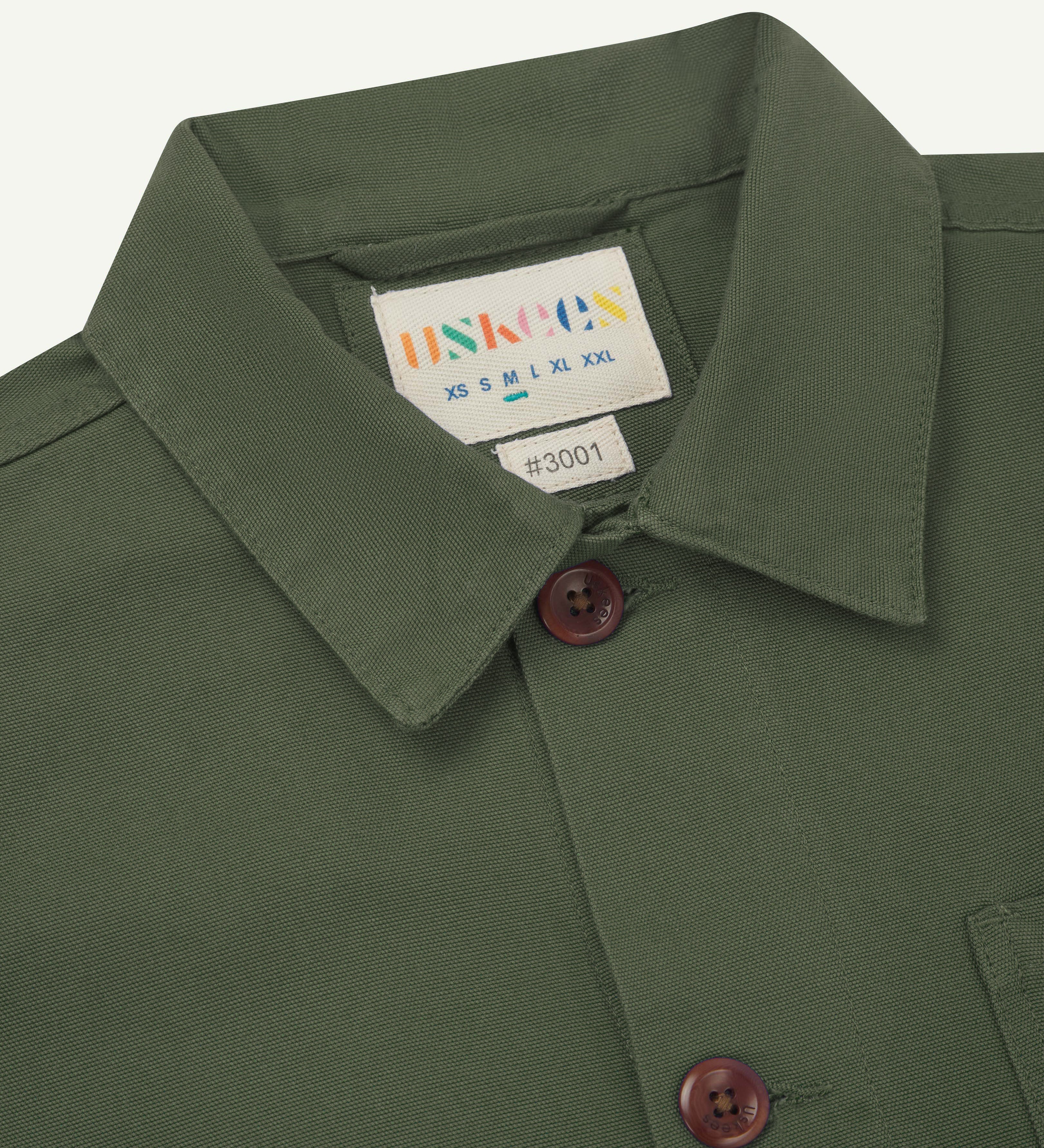 Front detail shot of  the neck and front buttons of a coriander green men's overshirt  showing the uskees brand  label