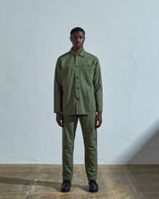 Full-length front view of model wearing #3001, coriander-green organic cotton overshirt paired with dark pants.