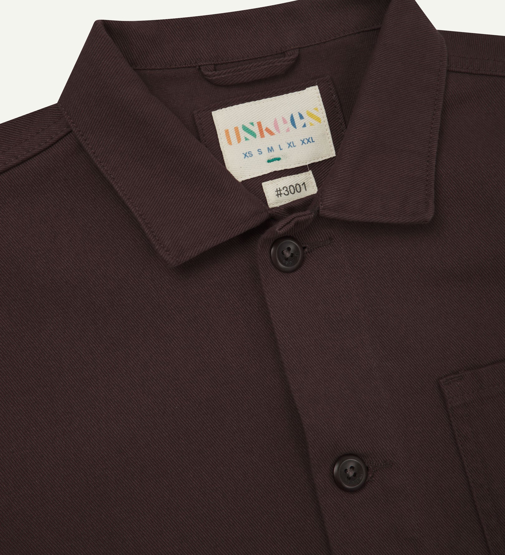 Close-up top-half view of #3001, burgundy-brown organic cotton drill overshirt. With focus on collar, Uskees brand label and corozo buttons.