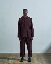 Full-length front view of model wearing #3001 dark plum-coloured organic cotton-drill overshirt, showing secured corozo buttons and paired with matching Uskees pants.