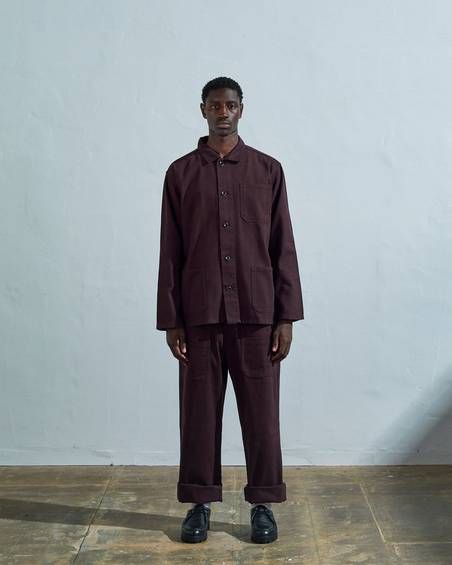 Full-length front view of model wearing #3001 dark plum-coloured organic cotton-drill overshirt, showing secured corozo buttons and paired with matching Uskees pants.
