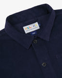 Close-up top-half view of #3001 deep indigo organic cotton corduroy overshirt. With focus on collar, hanging loop, Uskees brand label and corozo buttons.