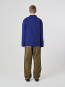 Full-length back view of man wearing an Uskees deep indigo cotton overshirt paired with khaki pants, showing reinforced elbows.