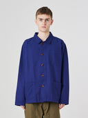 Top-half view of man wearing an Uskees deep indigo cotton overshirt indicating roomy, boxy fit with clear view of deep pockets on the chest and front.