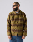 Model wearing Delph woodland green check, buttoned Pennine wool overshirt. Showing front and paired with jeans.