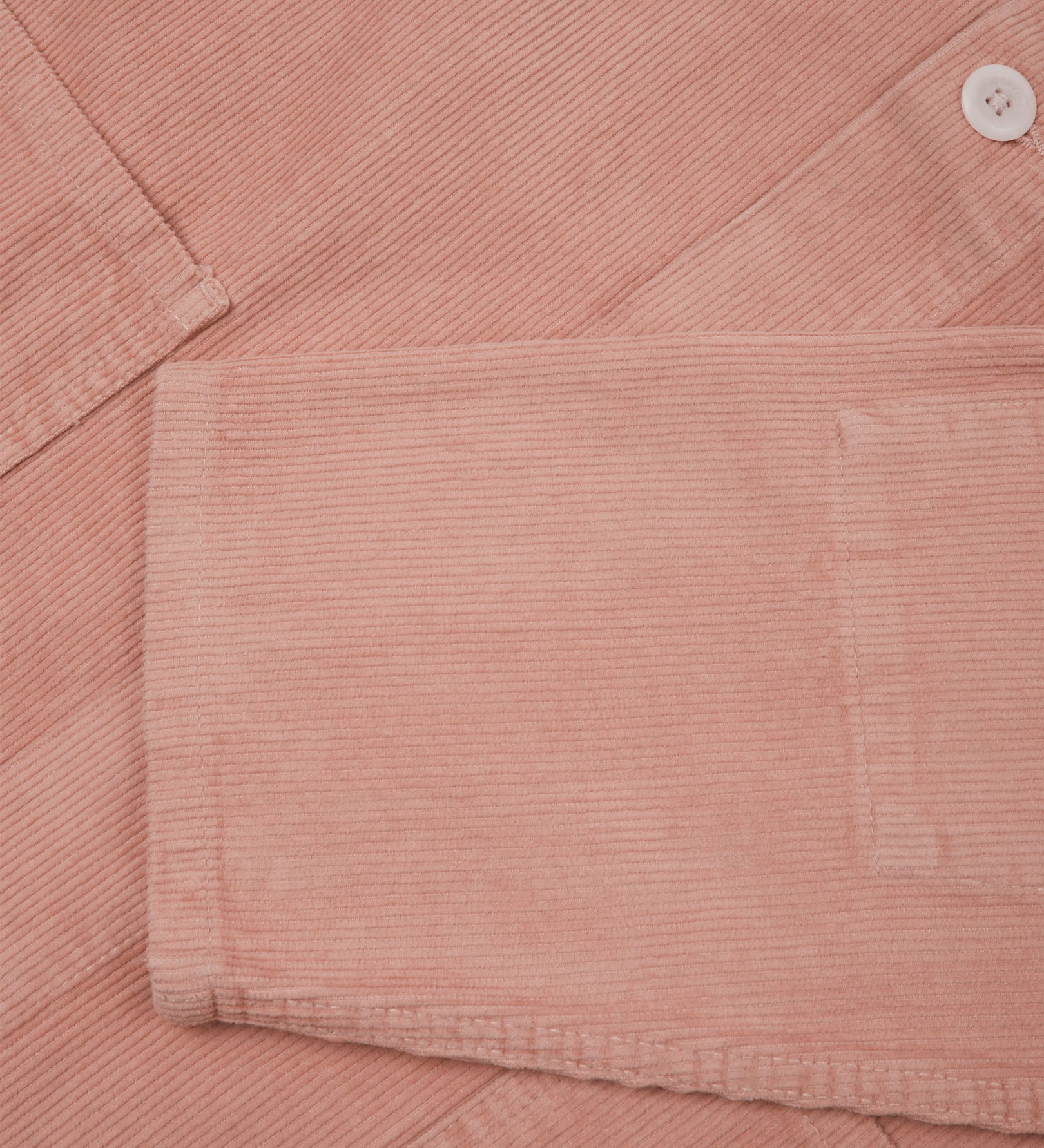 Closer view of mid section of dusty pink, buttoned corduroy overshirt from Uskees. Focus on cuff, pockets, corozo buttons and corduroy texture.
