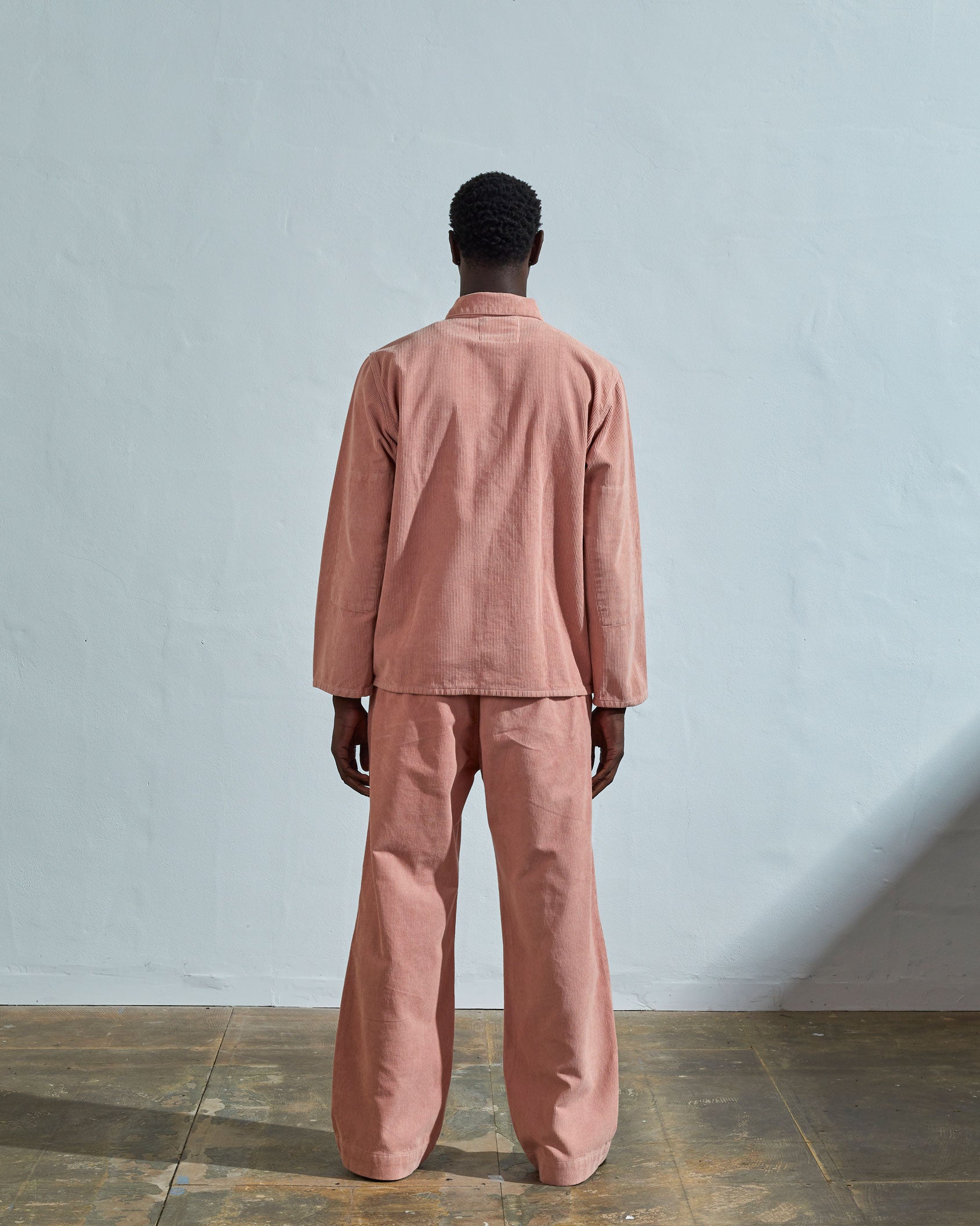 Full-length reverse view of model wearing #3001, dusty pink corduroy overshirt with view of reinforced elbow area and demonstrating boxy silhouette.