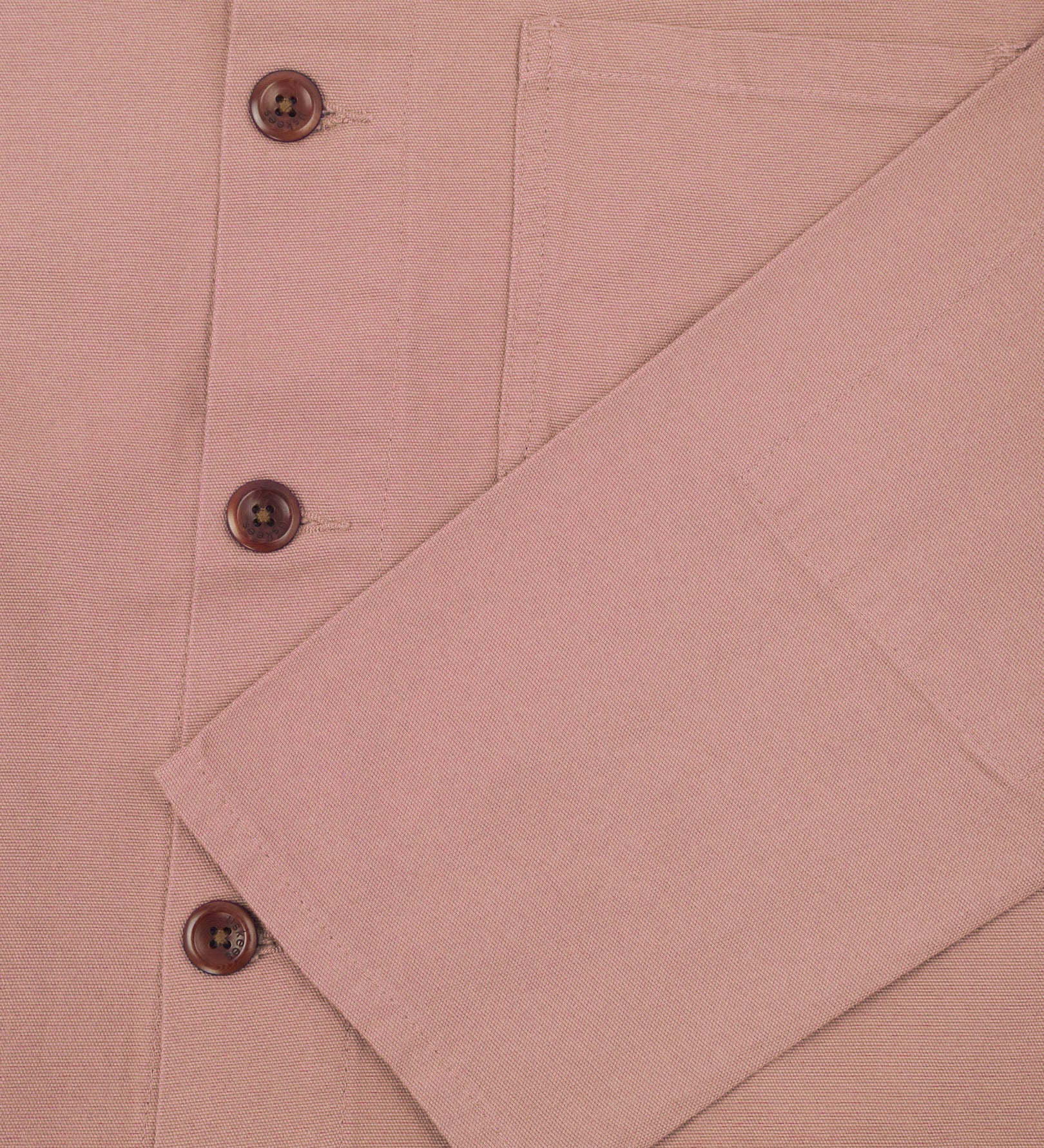 Closer view of mid section of dusty pink, buttoned organic cotton overshirt from Uskees. Focus on cuff, pockets and corozo buttons.