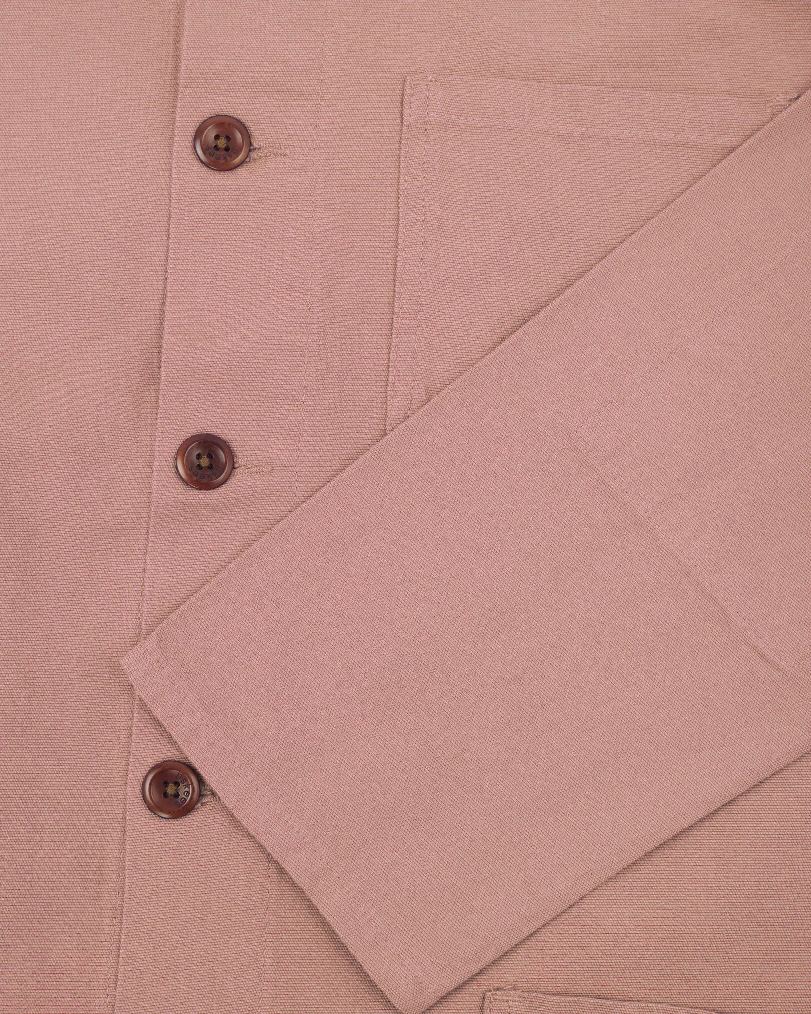 Closer view of mid section of dusty pink, buttoned organic cotton overshirt from Uskees. Focus on cuff, pockets and corozo buttons.