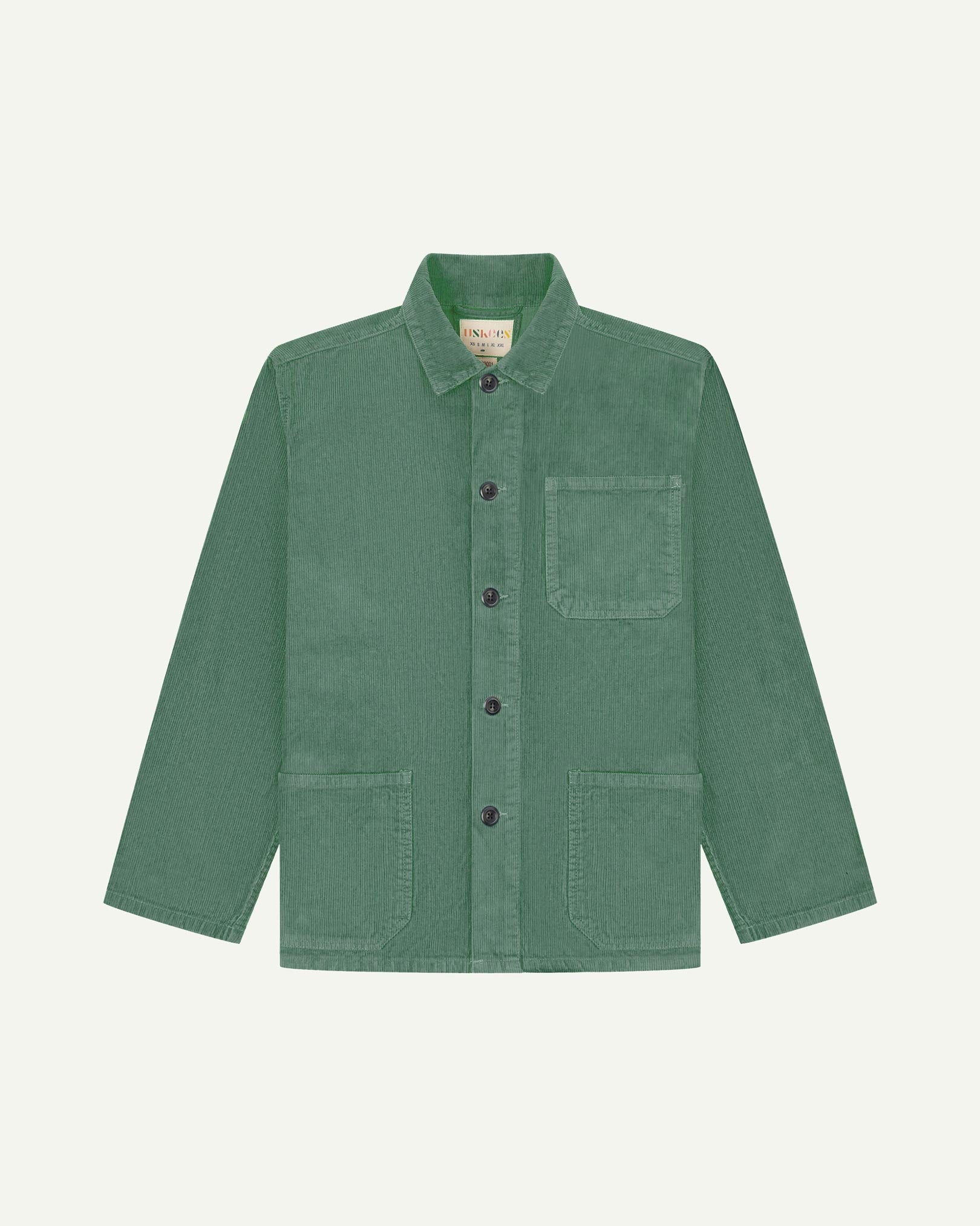 Front flat shot of light green, buttoned corduroy overshirt. Clear view of chest and hip pockets, corozo buttons and Uskees branding label.