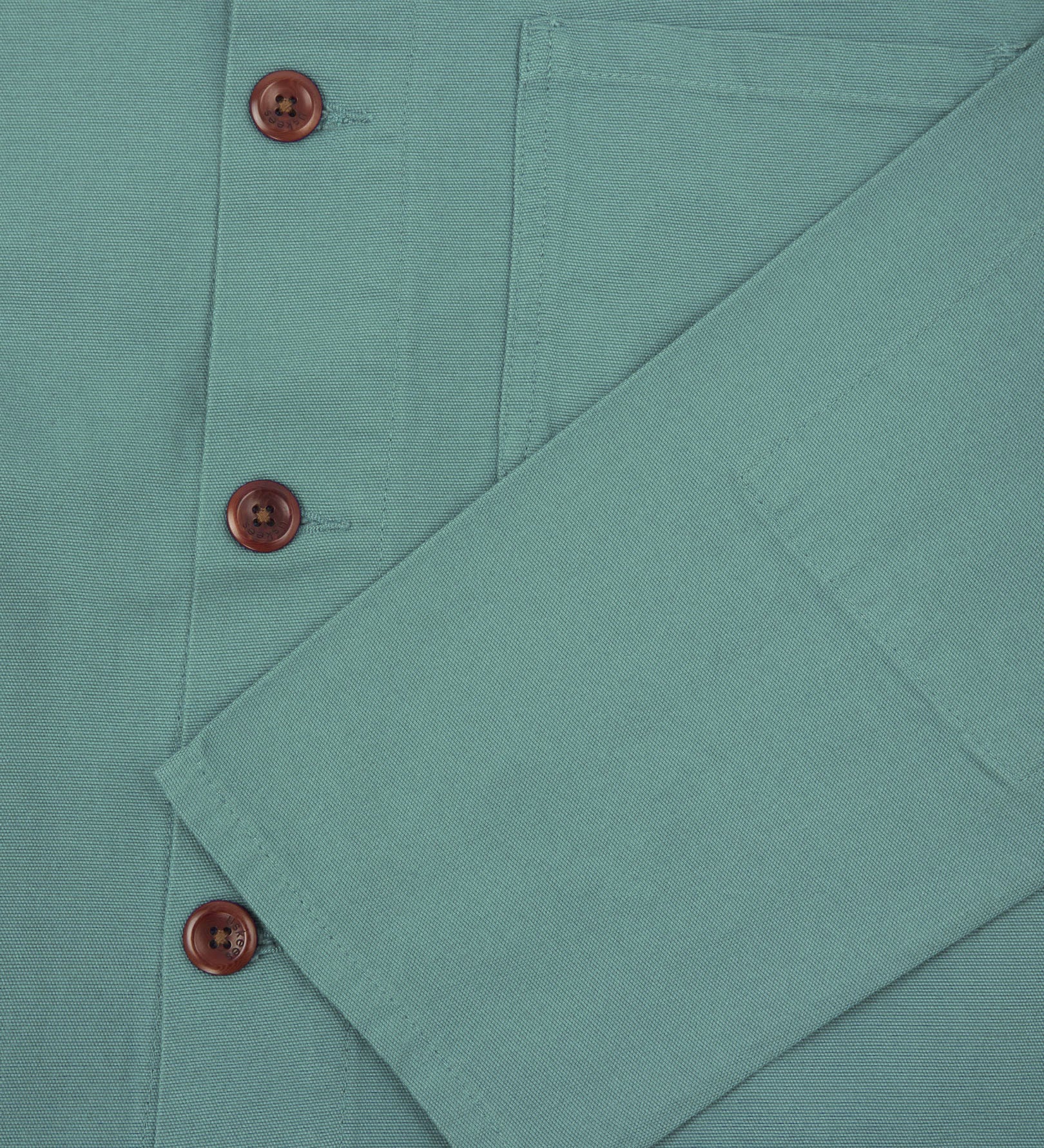 Closer view of mid section of blue-green (eucalyptus), buttoned organic cotton overshirt from Uskees. Focus on cuff, pockets and corozo buttons.