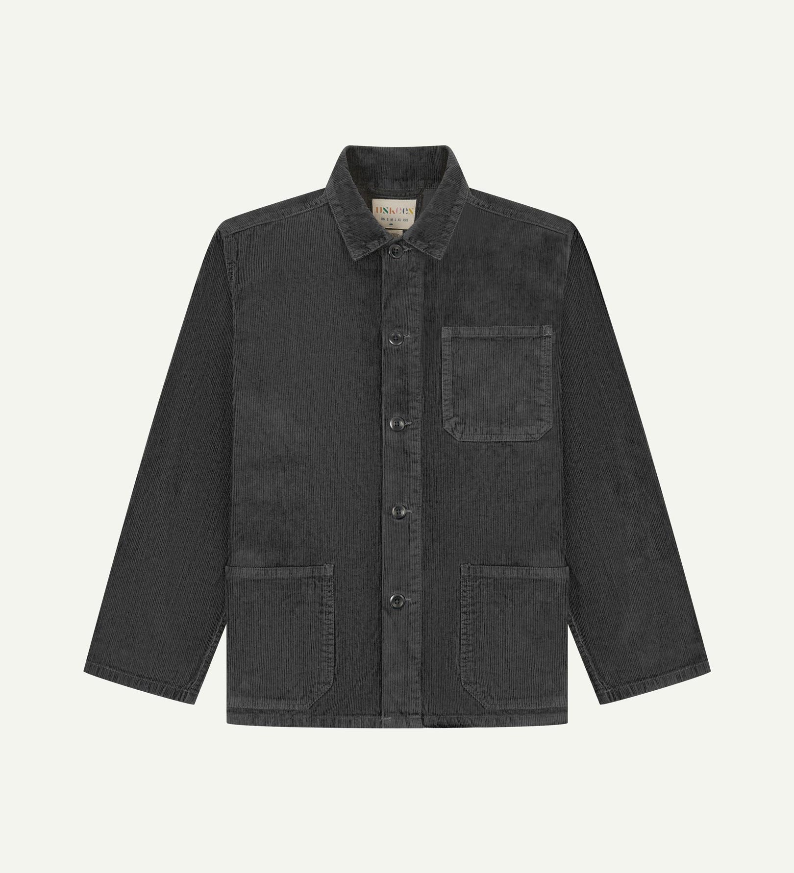 Front flat shot of faded black, buttoned corduroy overshirt. Clear view of chest and hip pockets, corozo buttons and Uskees branding label.