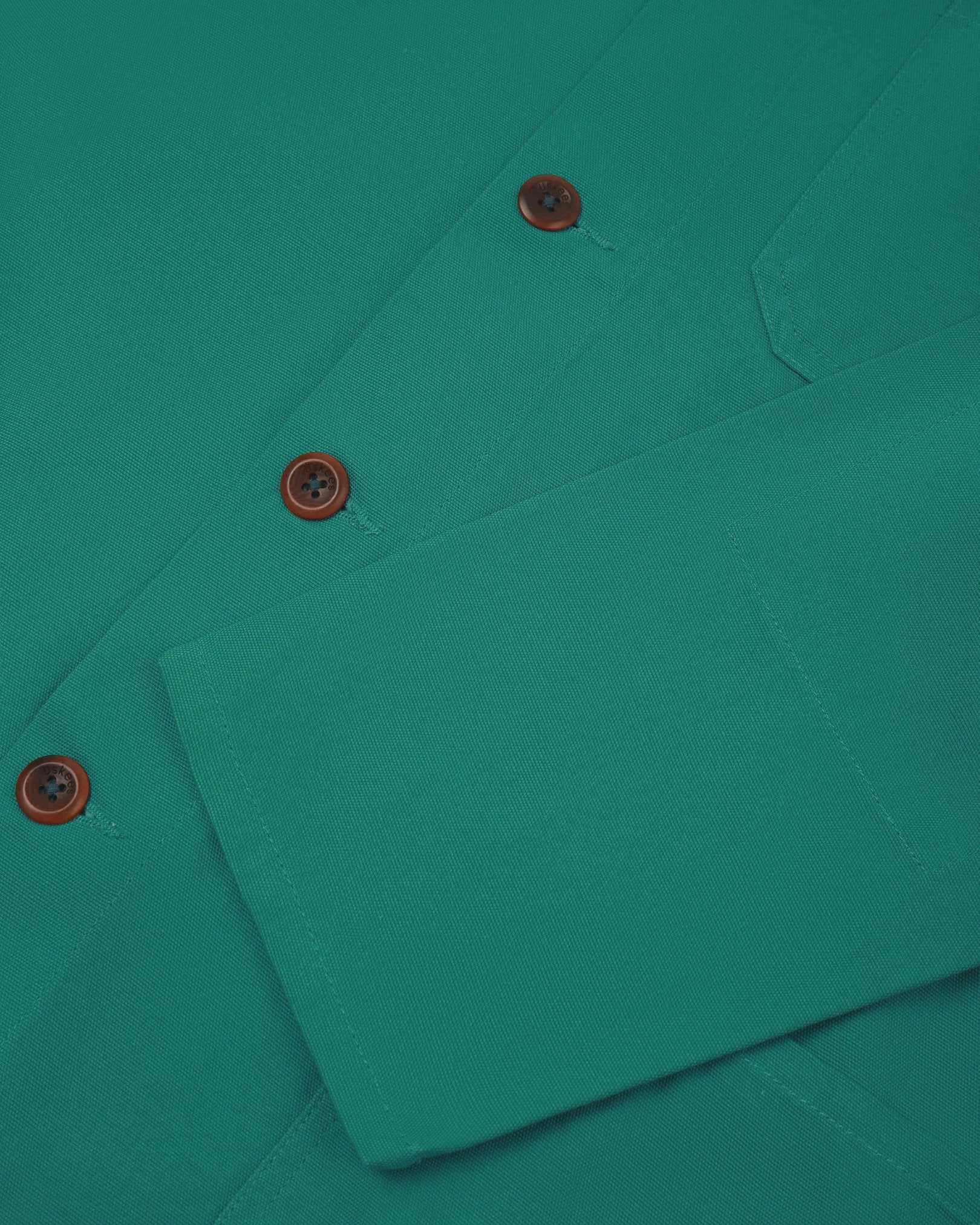 Closer view of mid section of foam green, buttoned organic cotton overshirt from Uskees. Focus on cuff, pockets and corozo buttons.