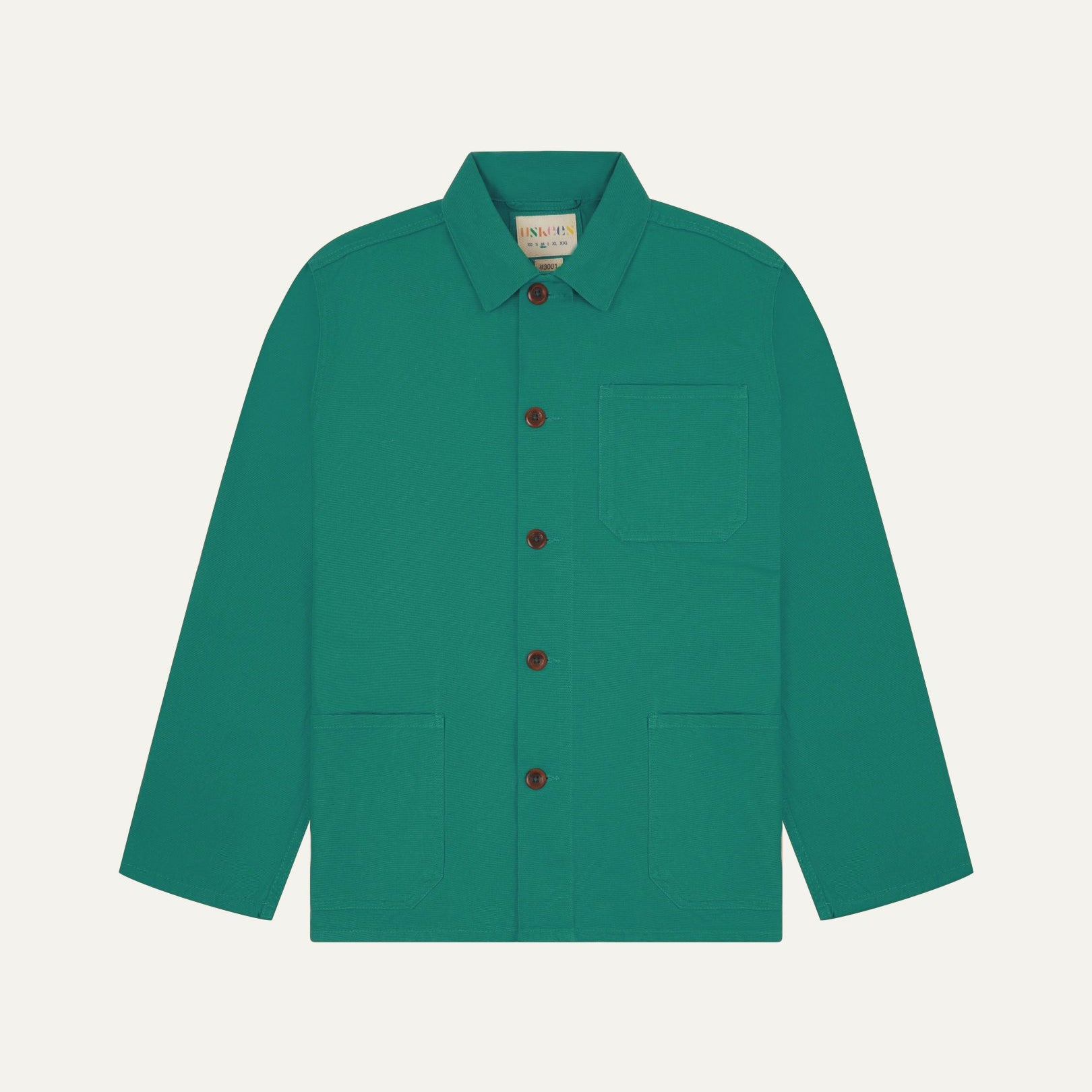 Front flat shot of foam green, buttoned organic cotton overshirt. Clear view of chest and hip pockets, corozo buttons and Uskees branding label.