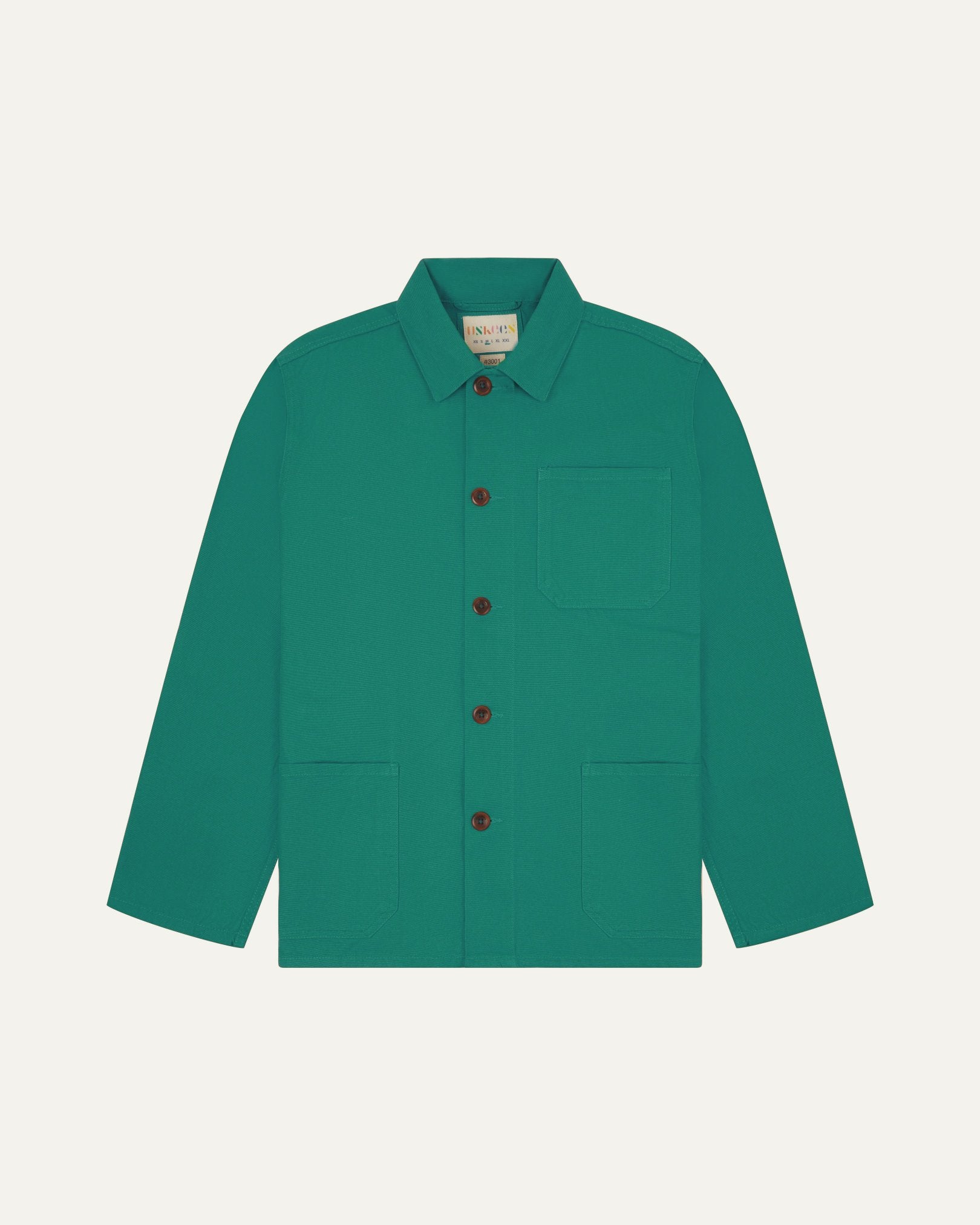 Front flat shot of foam green, buttoned organic cotton overshirt. Clear view of chest and hip pockets, corozo buttons and Uskees branding label.