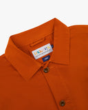 Close-up view of 3001 golden-orange, buttoned organic cotton overshirt from Uskees showing corozo buttons, brand label, collar and hanging hoop.