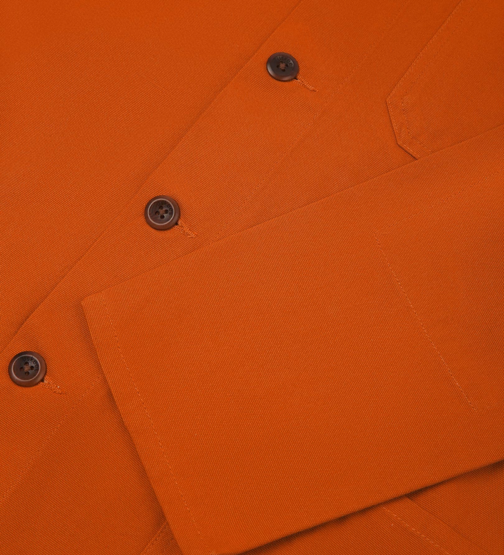Closer view of mid section of golden-orange, buttoned organic cotton overshirt from Uskees. Focus on cuff, pockets and corozo buttons.