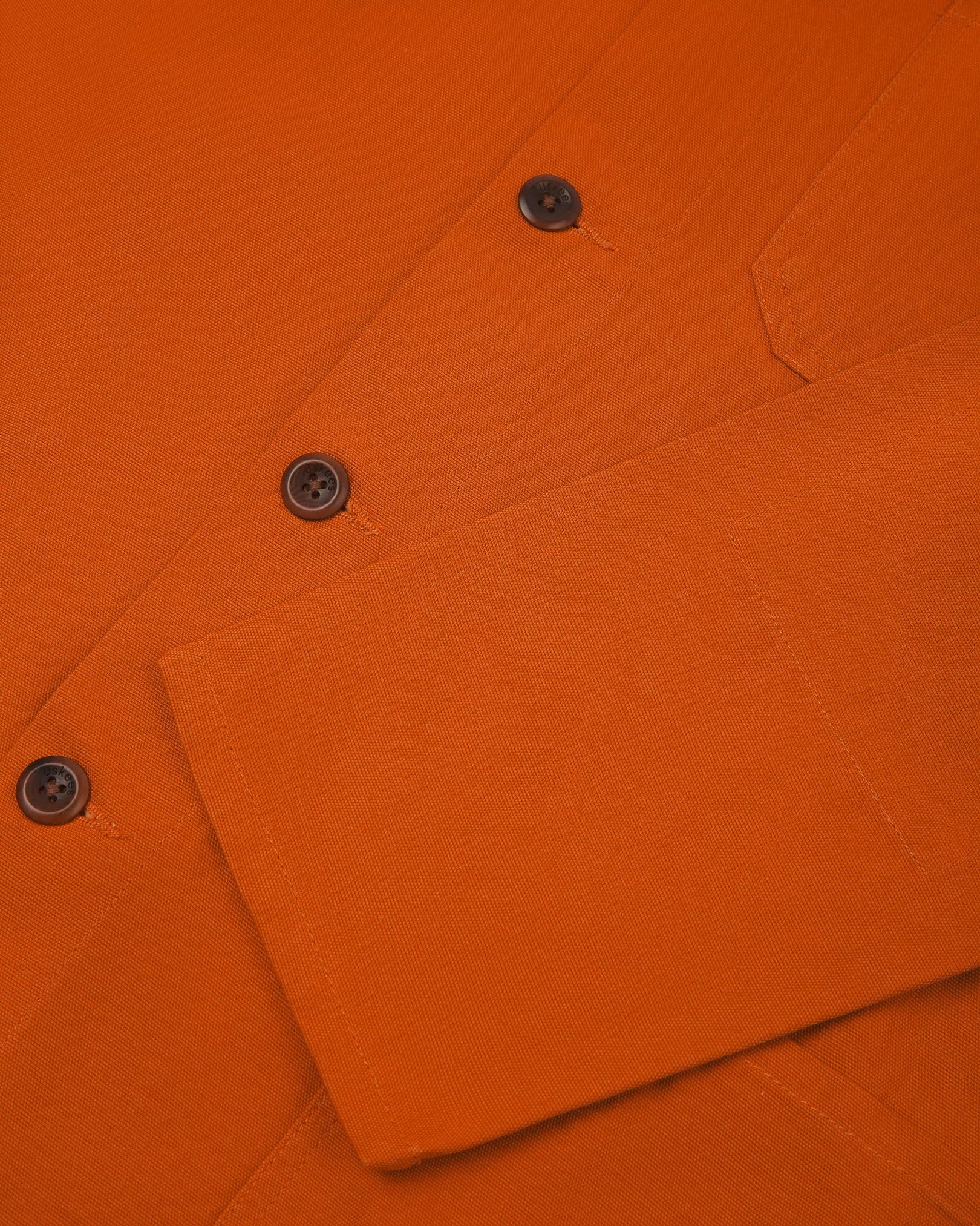 Closer view of mid section of golden-orange, buttoned organic cotton overshirt from Uskees. Focus on cuff, pockets and corozo buttons.