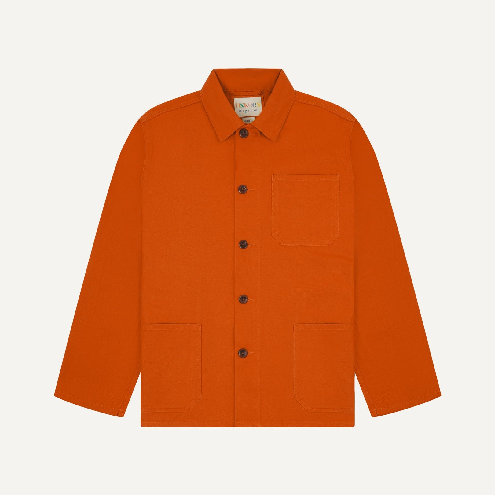 Front flat shot of golden-orange, buttoned organic cotton overshirt. Clear view of chest and hip pockets, corozo buttons and Uskees branding label.