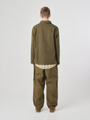 Full-length back view of man wearing an Uskees olive green ripstop overshirt paired with dark pants, showing reinforced elbows.