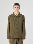 Top-half view of man wearing an Uskees olive green ripstop overshirt indicating roomy, boxy fit with clear view of deep pockets on the chest and front.