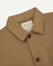 Close-up view of 3001 khaki, buttoned organic cotton overshirt from Uskees showing corozo buttons, brand label, collar and hanging hoop.