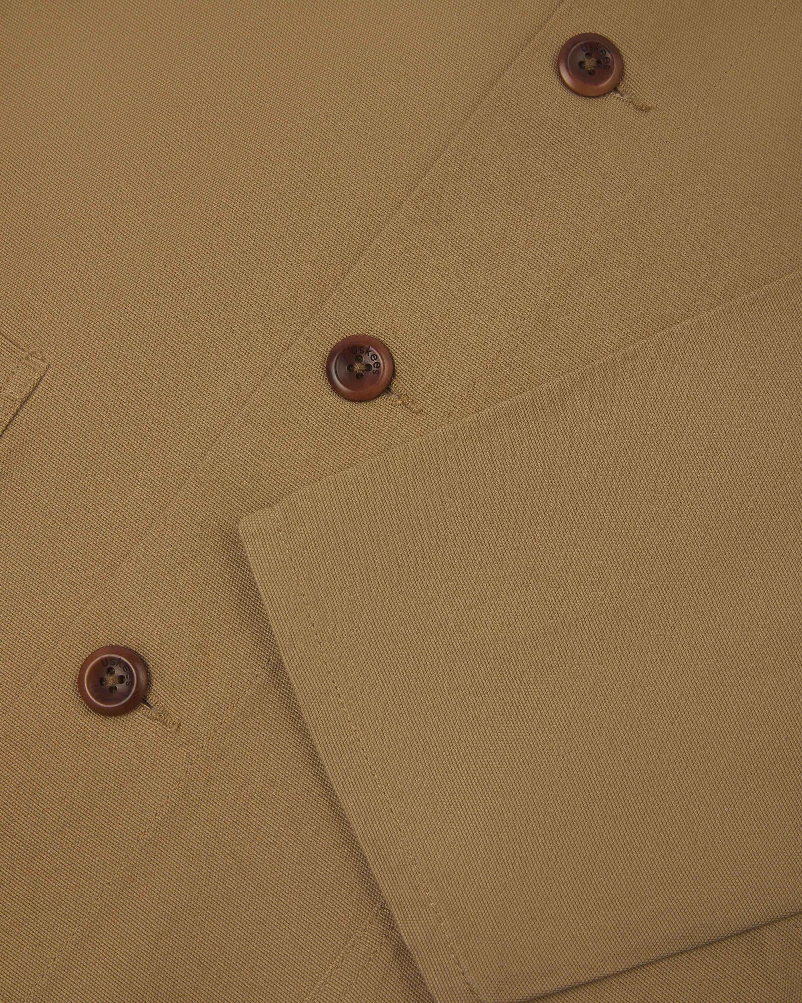 Closer view of mid section of khaki, buttoned organic cotton overshirt from Uskees. Focus on cuff, pockets and corozo buttons.