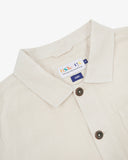 Close-up top-half view of #3001 off-white linen blend overshirt. With focus on collar, Uskees brand label and corozo buttons.
