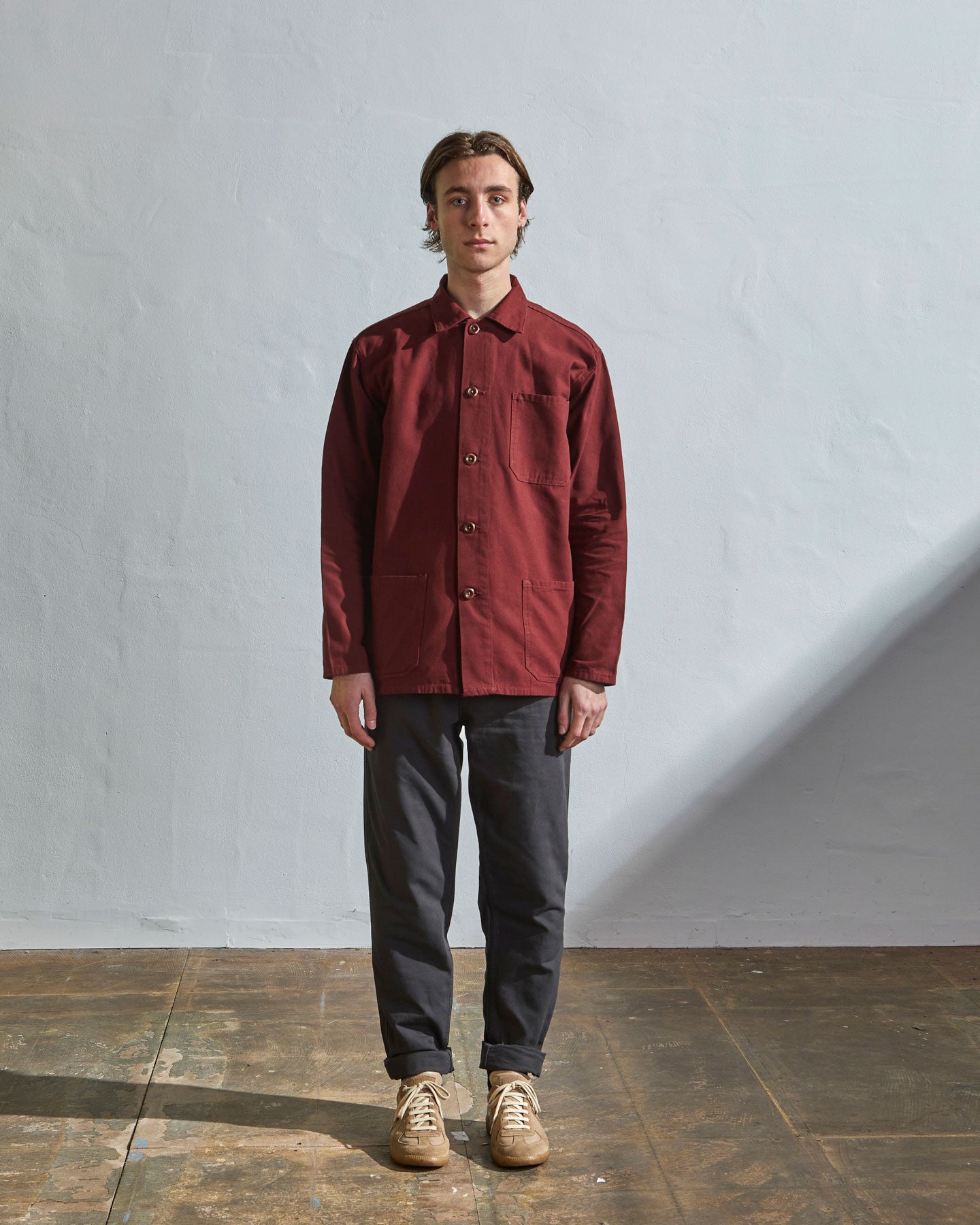 Full-length view of model wearing Uskees #3001 reddish-maroon overshirt showing utilitarian silhouette. Paired with charcoal pants.