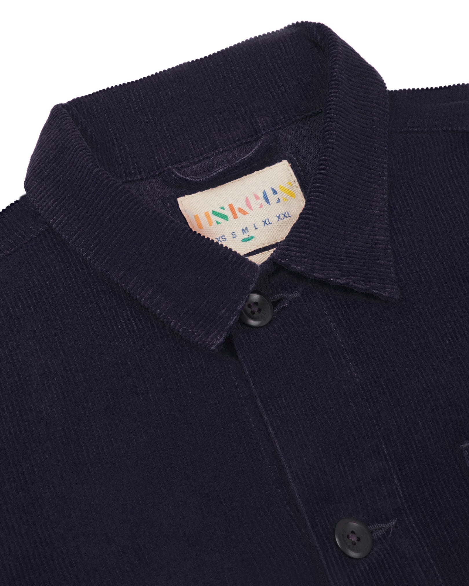 Close-up view of 3001 midnight blue, buttoned corduroy overshirt from Uskees showing corozo buttons, brand/size label, collar and hanging hoop.