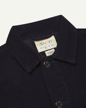 Close-up view of 3001 midnight blue, buttoned corduroy overshirt from Uskees showing corozo buttons, brand/size label, collar and hanging hoop.