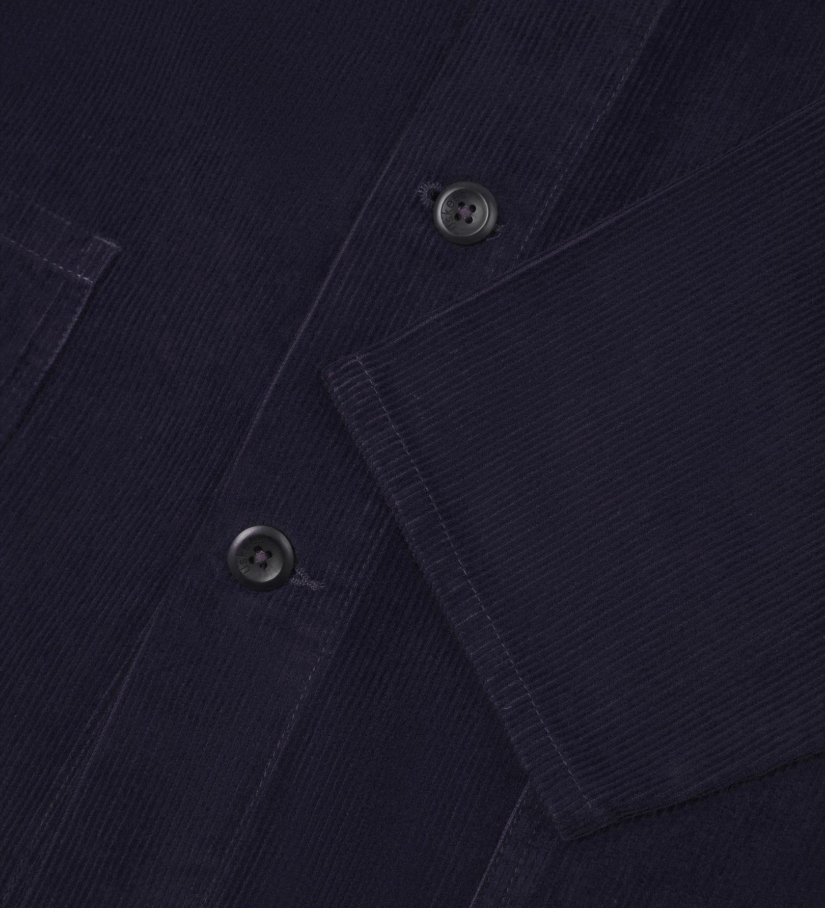 Closer view of mid section of midnight blue, buttoned corduroy overshirt from Uskees. Focus on cuff, pockets, corozo buttons and corduroy texture.