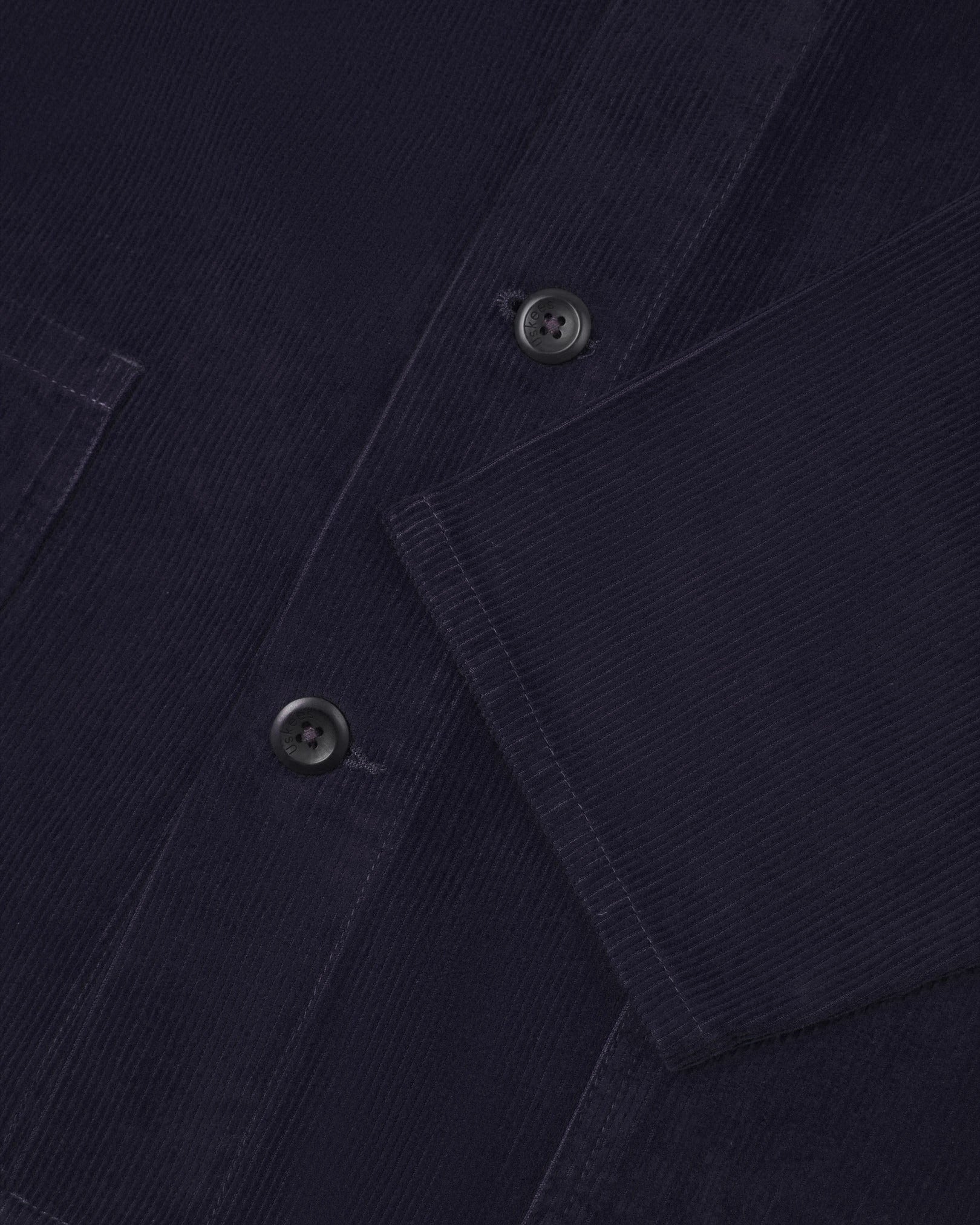 Closer view of mid section of midnight blue, buttoned corduroy overshirt from Uskees. Focus on cuff, pockets, corozo buttons and corduroy texture.