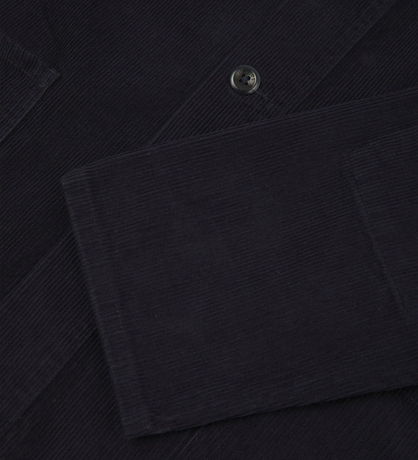 Closer view of mid section of midnight blue, buttoned corduroy overshirt from Uskees. Focus on cuff, pockets, corozo buttons and corduroy texture.
